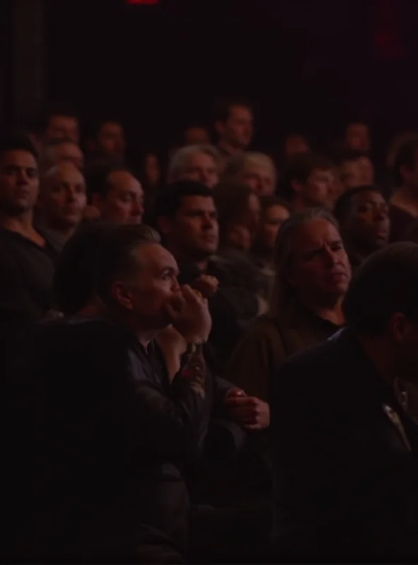 An audience reacting to a speaker, looking unimpressed and slightly bored.