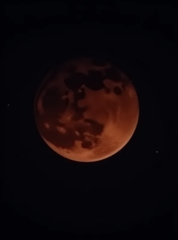 A vibrant total lunar eclipse, often called a blood moon, shining brightly in the night sky with stars visible in the background.