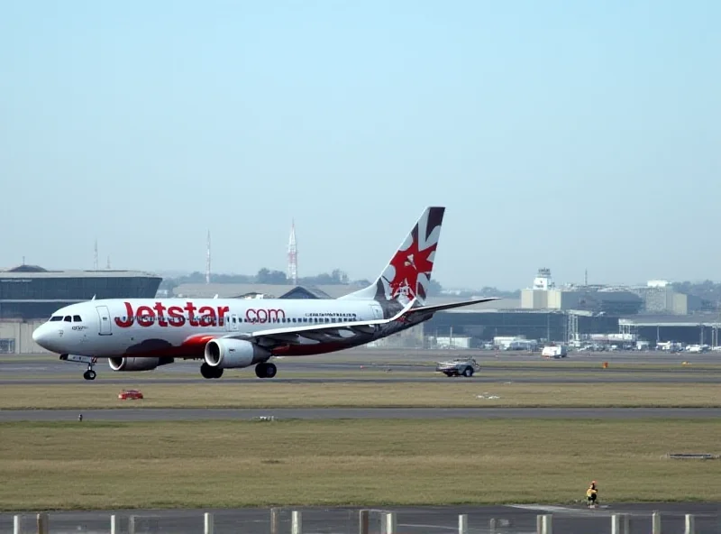 A Jetstar airplane on a runway with airport buildings in the background.