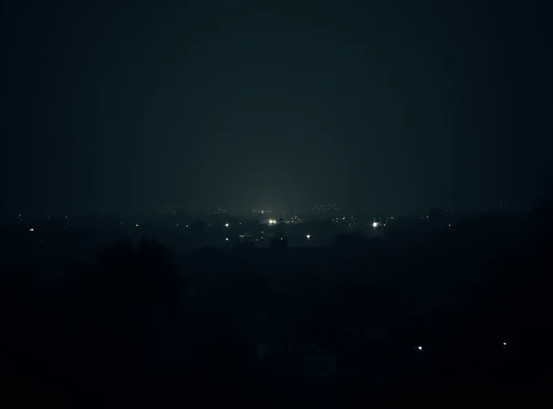 A darkened cityscape in Chile after a nationwide blackout. The sky is dark, and only a few scattered lights are visible in the distance. The scene conveys a sense of disruption and unease.