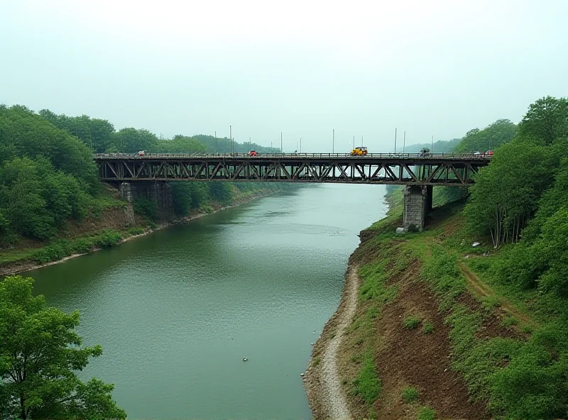 A partially constructed bridge spanning a wide river, with construction equipment and workers visible. The landscape around the river is green and lush.