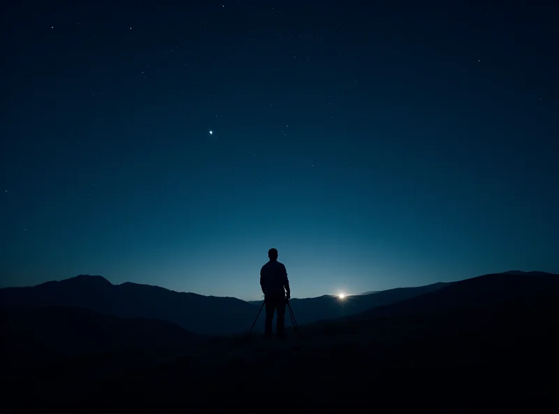 Wide angle view of a night sky above rolling hills, with several planets visible as bright points of light. A photographer stands silhouetted in the foreground.