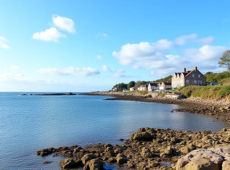 The coastline of Fife in Scotland, showing a rocky beach, blue sea, and a small village in the distance.